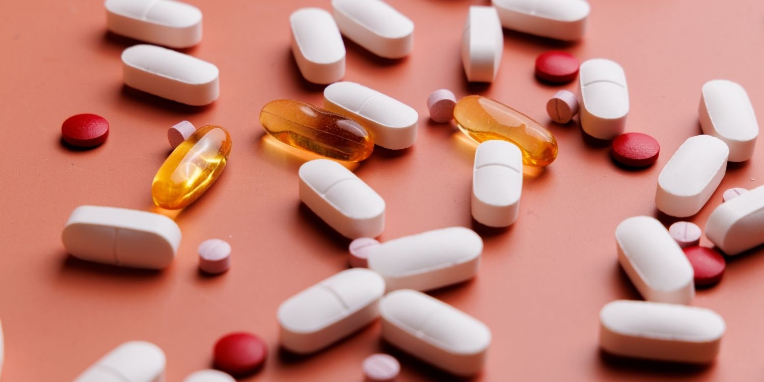 Auf einem altrosa Untergrund liegen verstreut weiße Tabletten, gelbe Kapseln sowie rosa und rote Pillen.. Artikel "Nahrungsergänzungsmittel oder Arzneimittel" öffnen.