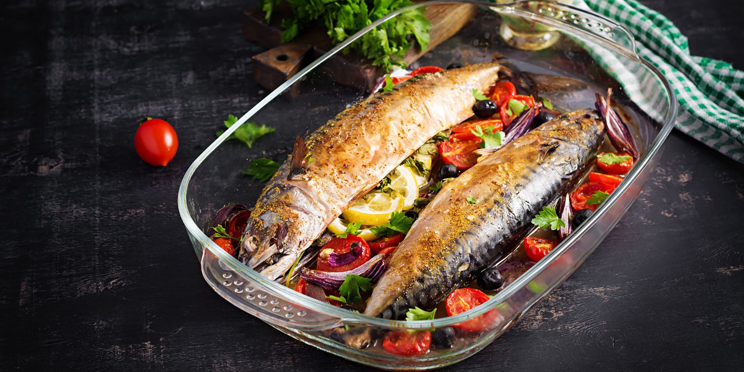 Auf einem dunklen Untergrund steht eine gläserne Ofenform mit zwei ganzen gebackenen Makrelen, Tomatenhälften, Zwiebeln, Kräutern und Zitronenscheiben darin.. Artikel "Hype um Omega-3-Fettsäuren" öffnen.