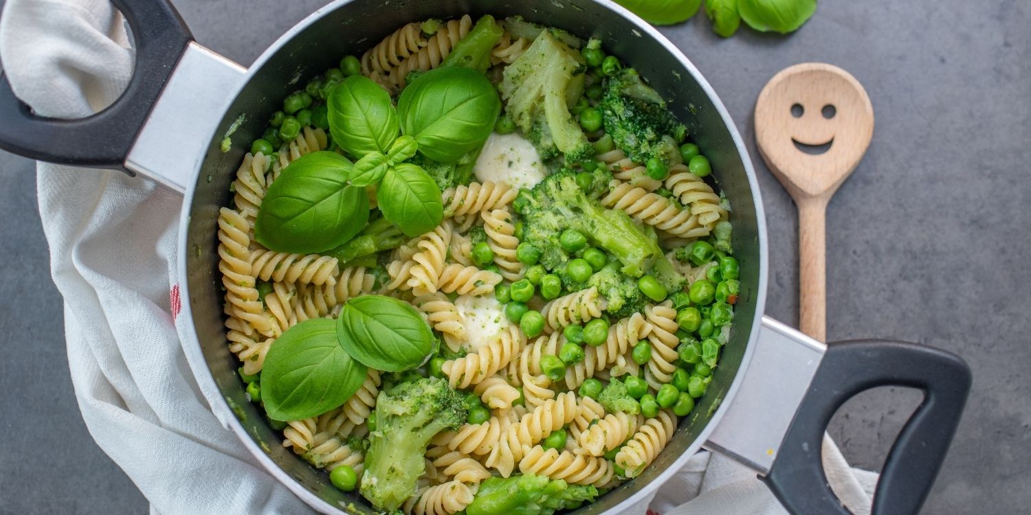 Auf einem grauen Tisch steht ein Topf mit gekochten Spiralnudeln, grünen Erbsen, Brokkoli, Mozzarella und frischem Basilikum garniert.. Artikel "One-Pot-Gerichte – alles aus einem Topf" öffnen.
