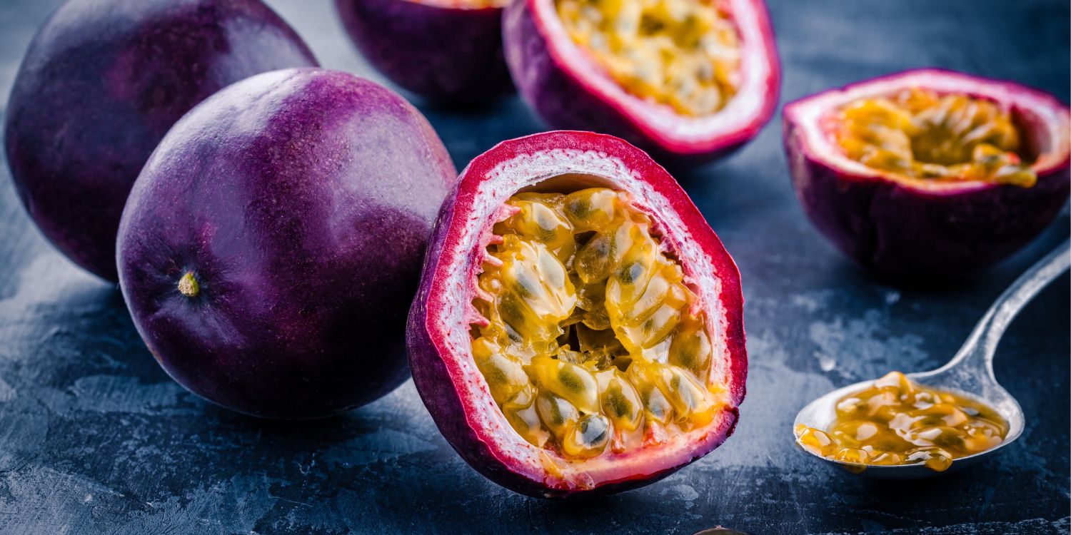 Auf einer dunklen Platte liegen ganze und halbierte violette Passionsfrüchte. Ein Löffel mit Fruchtfleisch liegt daneben. . Artikel "Exotische Frucht: Passionsfrucht" öffnen.