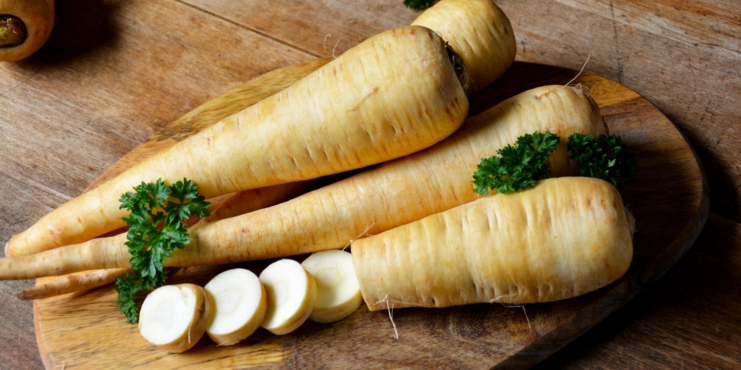 Auf einem Holzbrett liegen vier Pastinaken, eine davon ist zum Teil in Scheiben geschnitten.. Artikel "Pastinake für die Winterküche" öffnen.