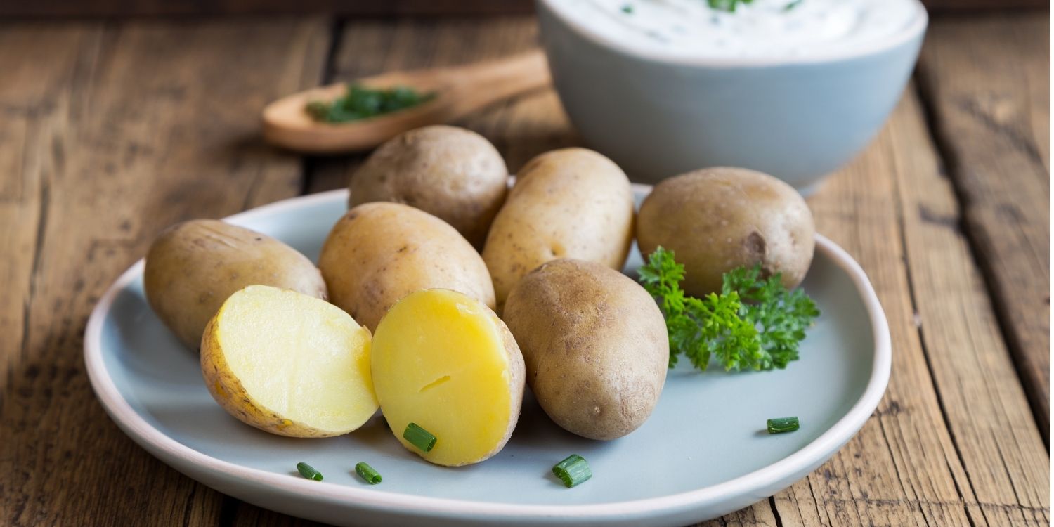 Auf einem dunklen Holztisch steht ein weißer Teller mit ganzen und halbierten Pellkartoffeln, daneben eine Schale mit Kräuterquark.. Artikel "Serafina, Marabel oder Karlena?" öffnen.