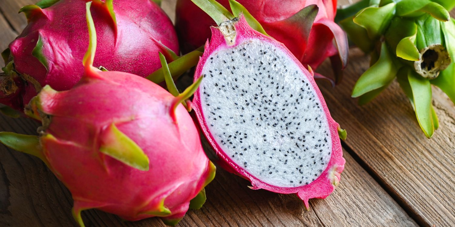 Mehrere ganze und eine halbierte Pitaya liegen auf einem dunklen Holzuntergrund.. Artikel "Warenkunde zum Mitnehmen" öffnen.