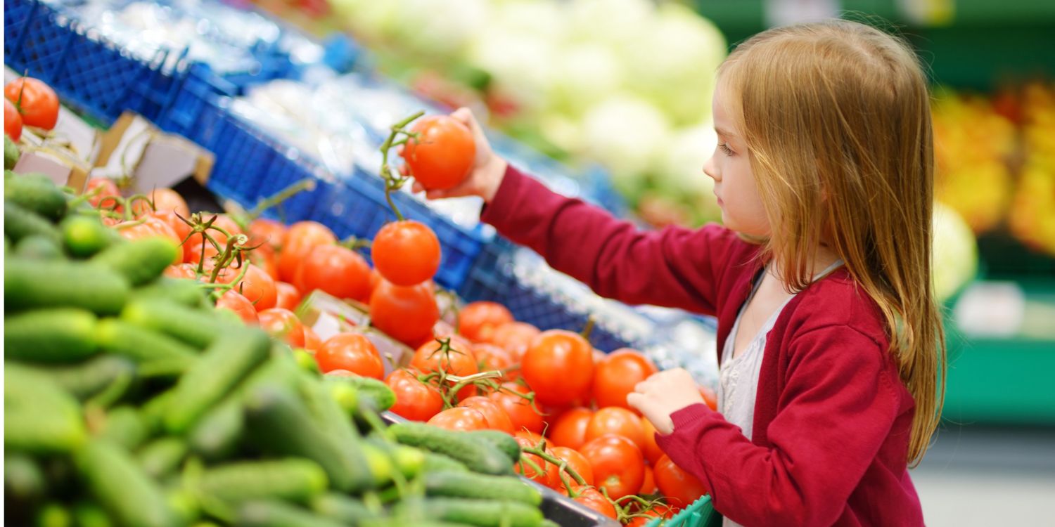 Ein Mädchen im Grundschulalter steht an einer Gemüsetheke im Supermarkt und betrachtet prüfend eine Tomate in ihrer Hand.. Artikel "Projekttage unterstützen Ernährungsbildung" öffnen.