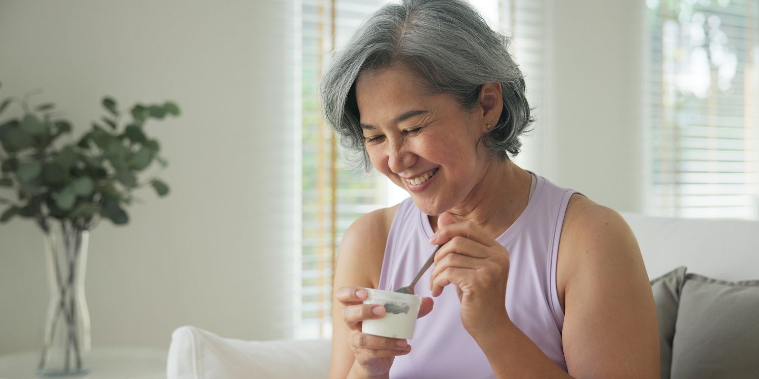 Eine etwa 50-jährige Frau isst einen Joghurt. . Artikel "Mehr Protein in den Wechseljahren?" öffnen.