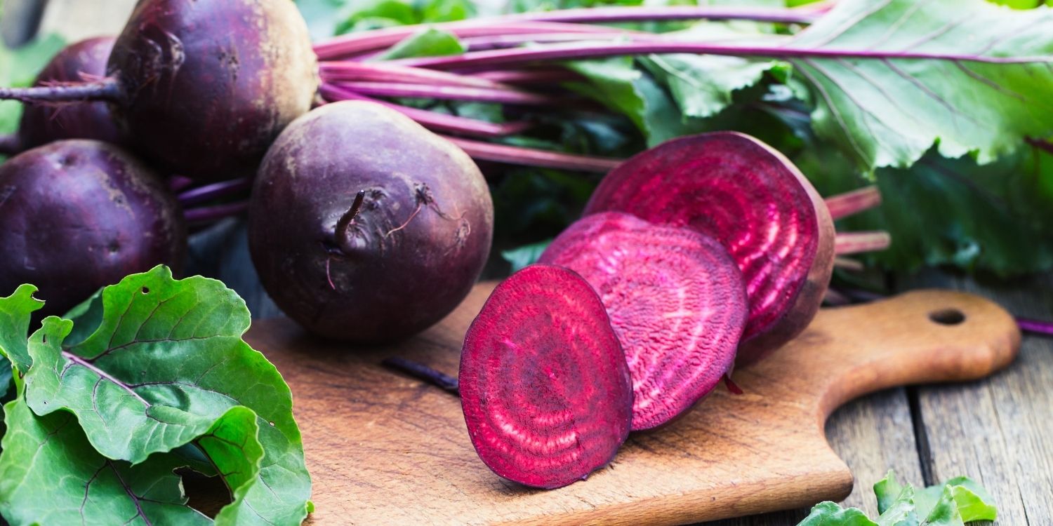 Auf einem Holzbrett liegen rote Beteknollen mit Blättern daran und eine Rote Bete ist in Scheiben geschnitten.. Artikel "Rote Bete – eine Knolle mit Charakter"" öffnen.