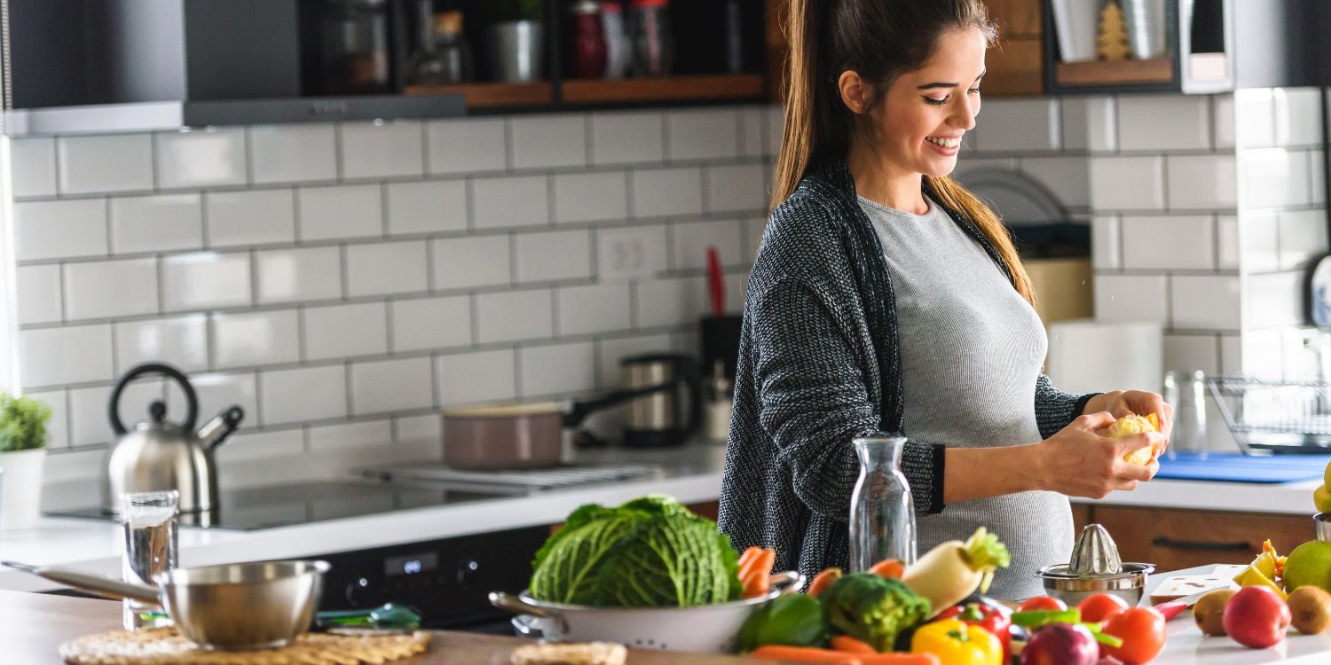 Eine schwangere Frau bereitet in ihrer Küche zu Hause gesundes Essen mit viel Obst und Gemüse zu.. Artikel "Besser essen in der Schwangerschaft" öffnen.