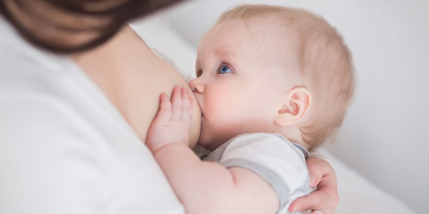 Ein älterer Säugling trinkt an der Brust und schaut zur Mutter auf.. Artikel "Wie lange soll gestillt werden?" öffnen.