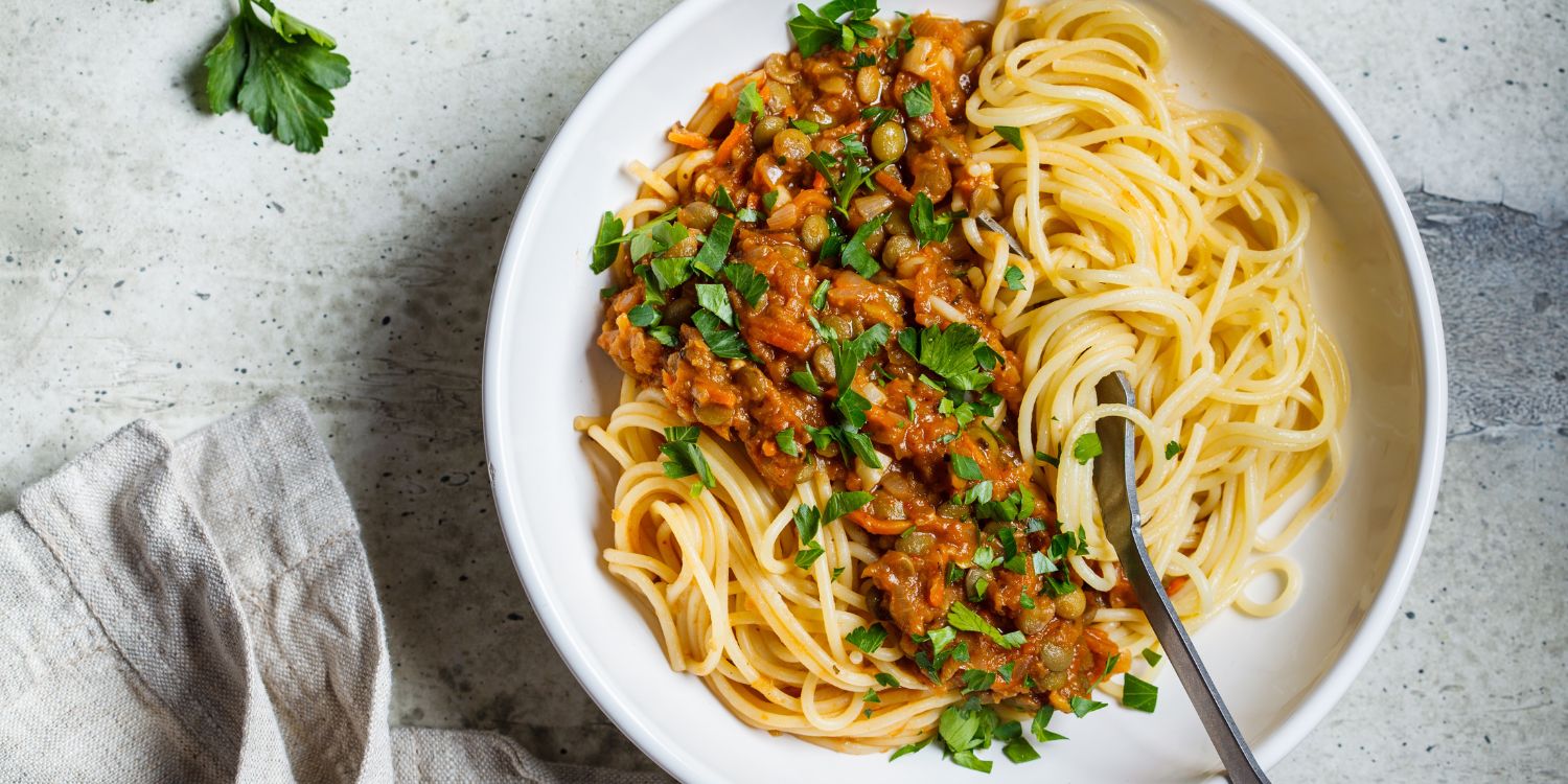 Auf einem weißen Teller ist vegetarische Linsen-Bolognese mit Pasta und Petersilie angerichtet.. Artikel "Tellerlinsen perfekt zubereiten" öffnen.