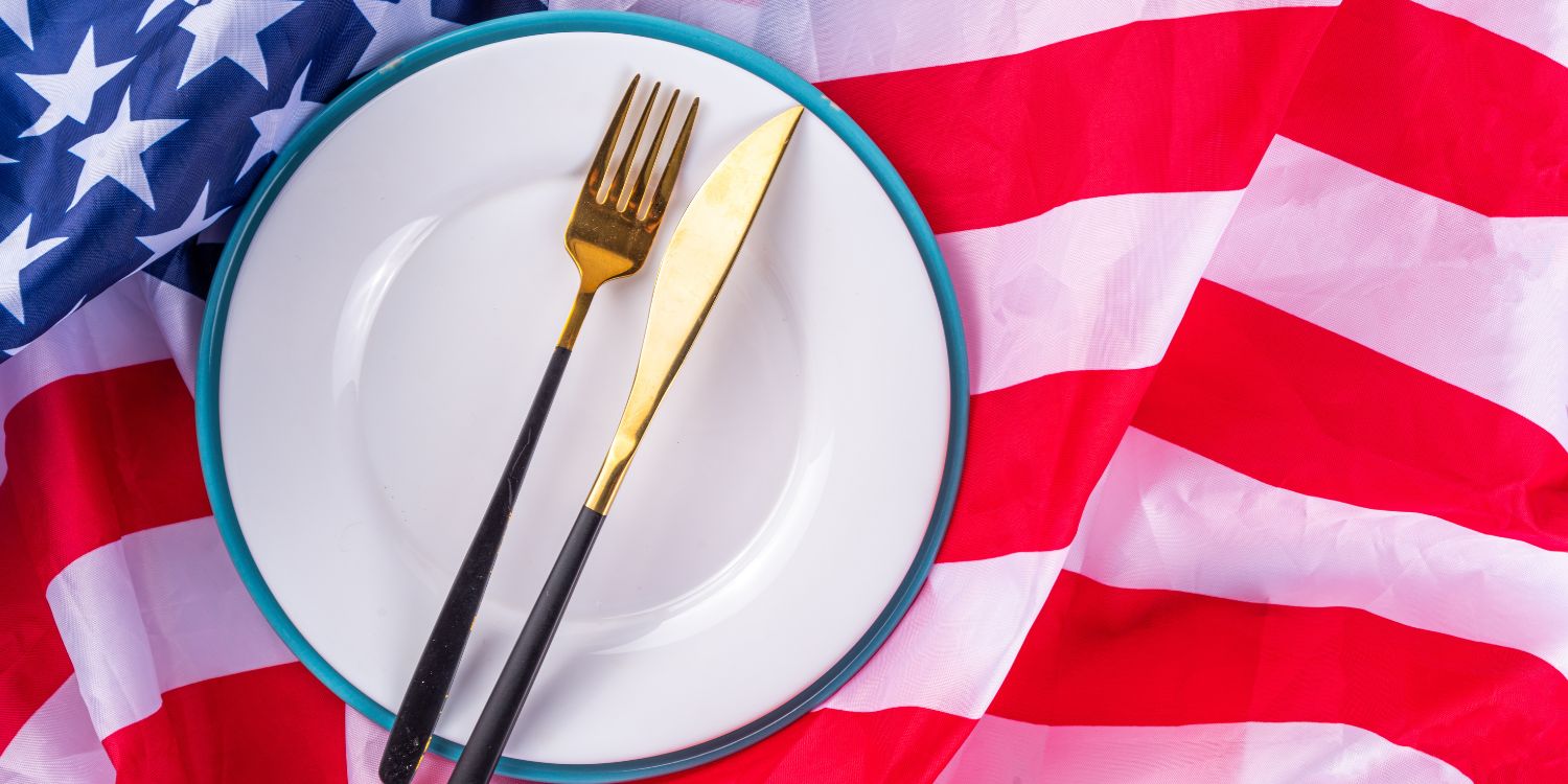 Auf einer US-amerikanischen Flagge liegt ein weißer Teller mit Messer und Gabel.. Artikel "Die Ernährungspyramide auf den Kopf gestellt" öffnen.