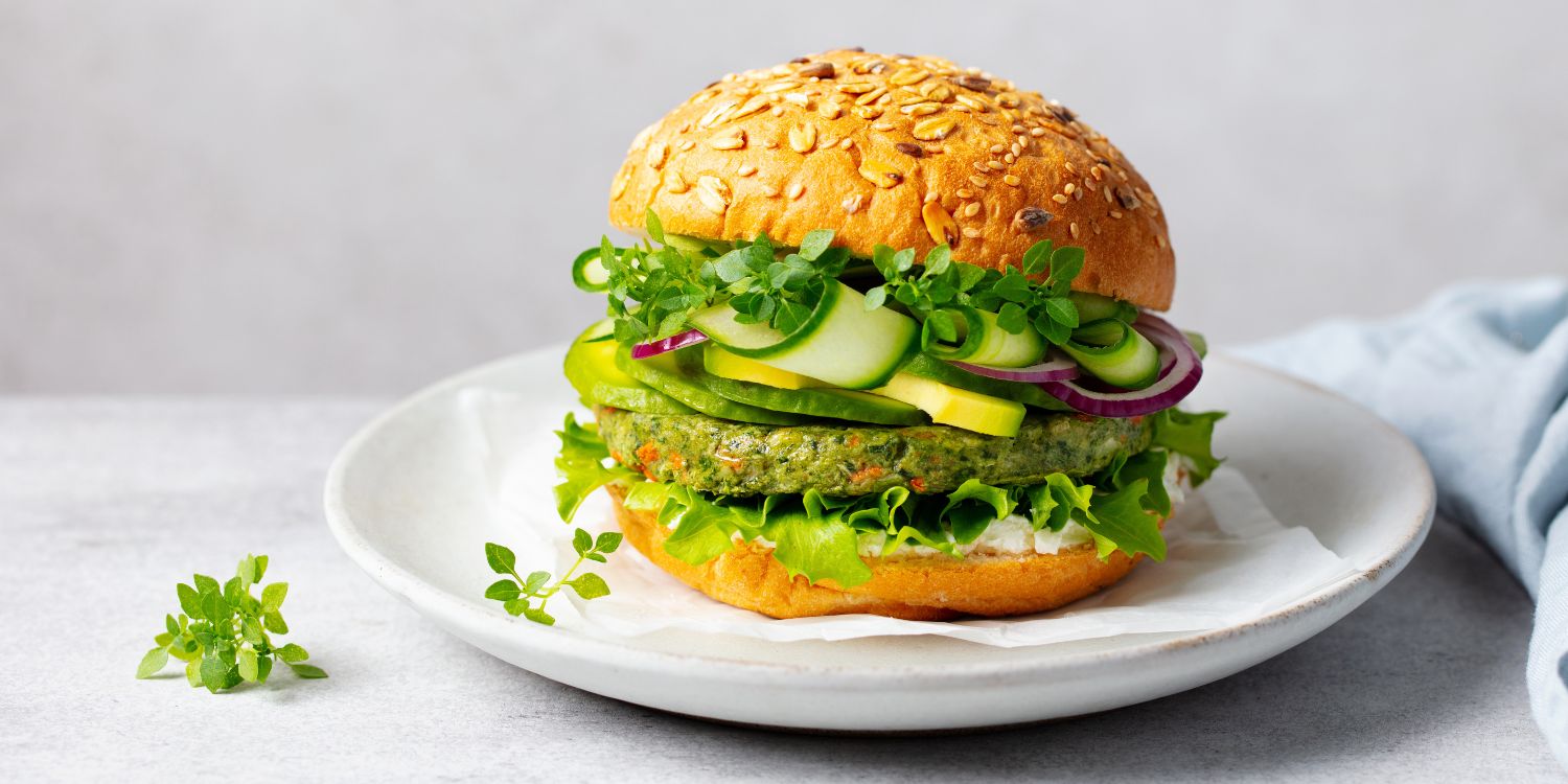 Auf einem weißen Teller liegt ein Burger mit einem Gemüsepatty, Gurken und Kräutern.. Artikel "Aus für Veggie-Steak und veganes Filet" öffnen.
