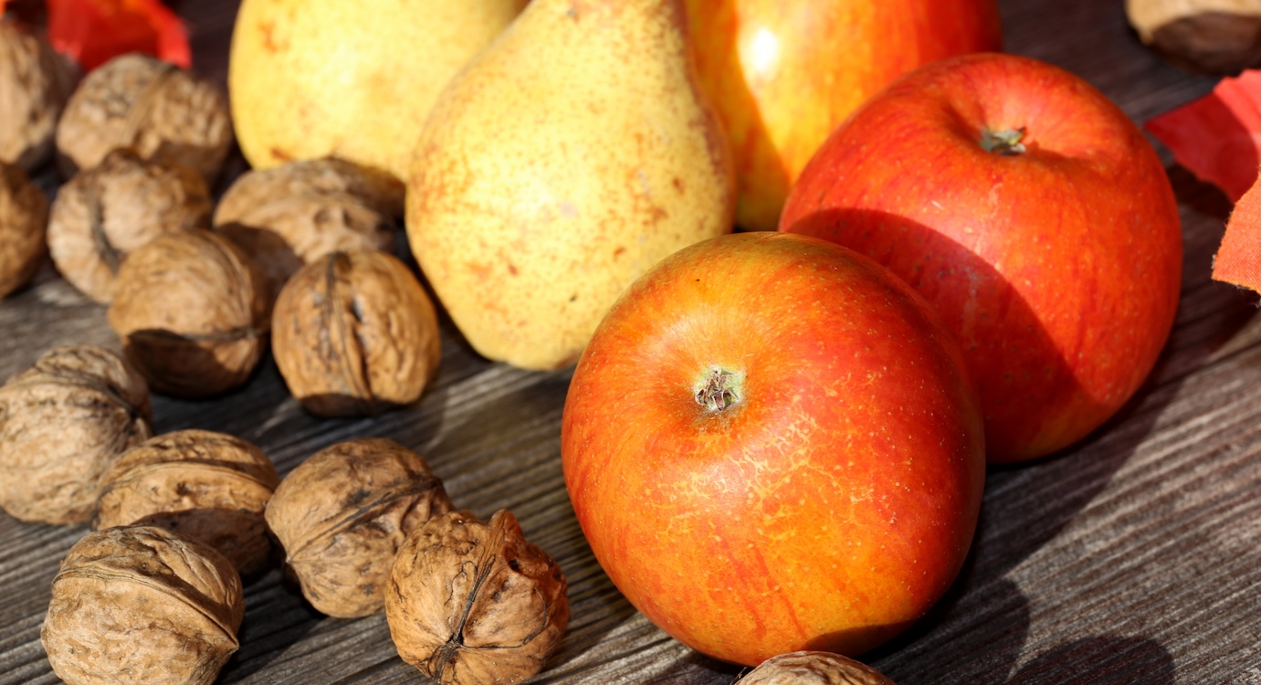 Äpfel, Walnüsse und Birnen liegen auf einem rustikalen Holztisch.. Artikel "Was ist Obst der Saison?" öffnen.